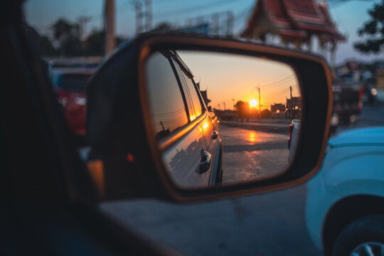 Sunset reflection in a car side mirror on a city street in Thailand,A cinematic shot showing a vibrant golden sunset reflected in a car's rearview mirror. The reflection captures the sun low.