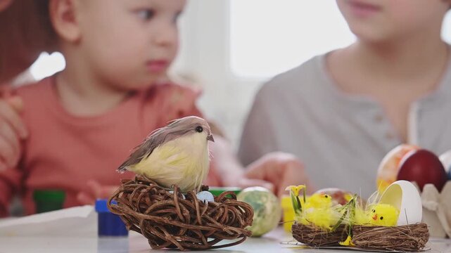 A close-up, selective focus, emphasis on the decor. Children color Easter eggs while sitting at a table decorated with Easter chicks in a nest. Birds in a nest craft.