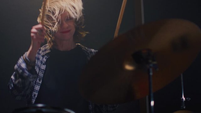 Young girl blonde rock is playing the drums on concert stage. Woman bangs on a drum kit. Face of female musician bangs drumsticks in a snare drum, cymbals in rehearsal studio, repetition. Portrait