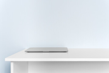 Closed laptop on white desk against blue wall with copy space