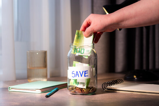 Close up of cash being added to transparent money jar. Represents traditional saving methods and conscious money management for future security