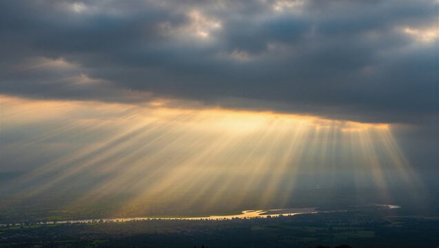 Sunlight streams through dark clouds, illuminating the landscape below with a golden hue. A breathtaking natural phenomenon showcasing the beauty of light and shadow.