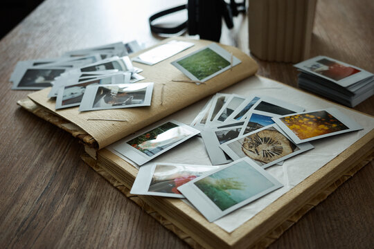 Collection of old photographs scattered on a wooden table with a camera nearby and a stack of more pictures beside them