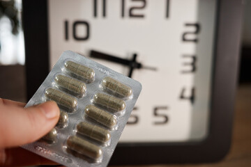 Obraz premium Man holds medicine in hand next to clock showing time for taking pills in a home setting during daylight