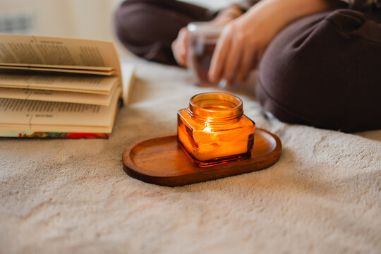Open book and burning candle on wooden tray over soft blanket. Intimate home setting with warm light. Concept of evening routine, relaxation, slow living and cozy autumn mood.