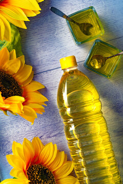 Botellas de aceite de girasol con decoraci&oacute;n floral.Botellas de aceite de girasol con recipientes de cristal, cucharas y girasoles sobre superficie azul. Concepto de ingrediente fresco y producto 