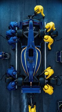 Top down shot blue formula race car surrounded by pit crew in yellow. Concept of competitive race logistics, precision tire service process, professional motorsport team performance.