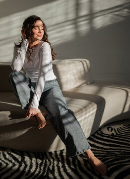 Woman seated on a sofa in a bright room with shadows on the wall