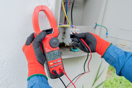 Close-up of an electrician's hands using a clamp meter to measure the flow of electric current