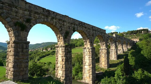 A multi-arched stone aqueduct spans a lush valley under a clear blue sky
