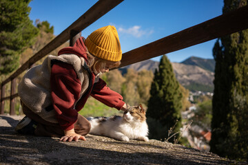 Little boy petting a cat on mountain viewpoint terrace, child and animal interaction, outdoor...