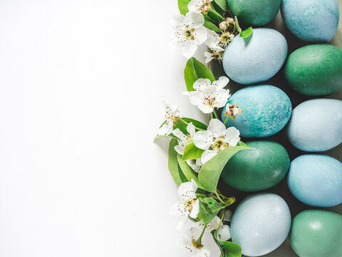 Pastel blue Easter eggs on a white table with spring blossoms. Festive Easter and spring celebration concept. Flat lay, minimalist style, copy space. Close-up, view from above
