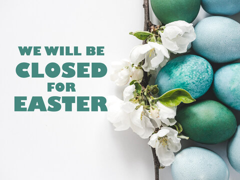 Signboard with We will be closed for Easter text. Pastel blue Easter eggs on a white table with spring blossoms. Festive Easter and spring celebration concept. Close-up, studio shot