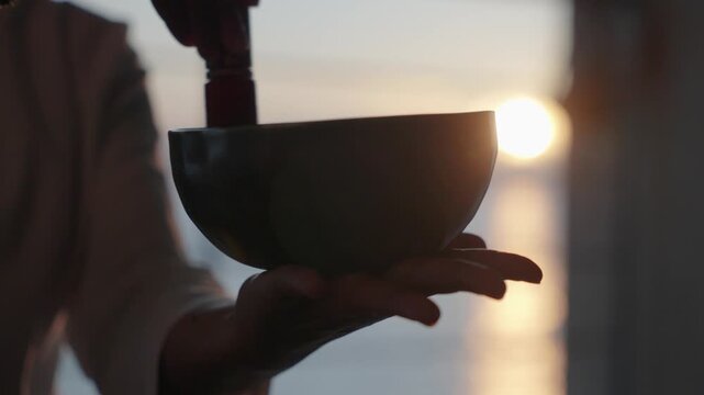 Silhouette of hands ringing a singing bowl at sunrise at a pavilion overlooking the ocean