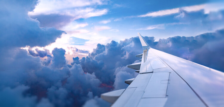 Ala de avi&oacute;n sobre las nubes durante un amanecer colorido.Vista del ala de un avi&oacute;n volando sobre nubes iluminadas con colores vibrantes de amanecer. Escena atmosf&eacute;rica de viaje y perspectiva a&eacute;rea.