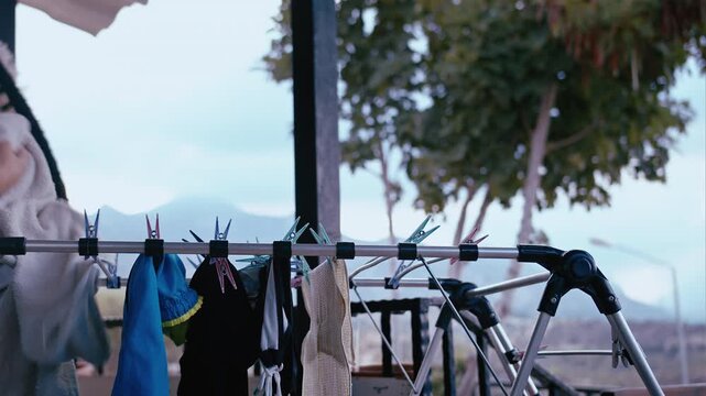 Woman Hanging Freshly Washed Laundry on Drying Rack at Home Veranda with Mountain View