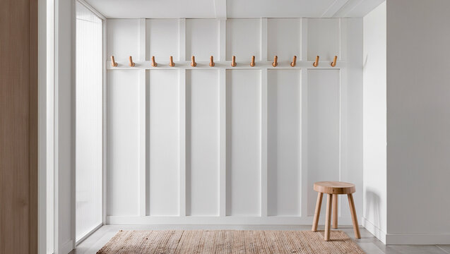 A clean interior with a white board and batten wall a row of ten wooden hooks a round wooden stool and a textured rug