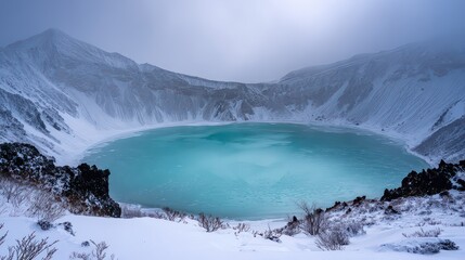 Crater Lake Turquoise Water Surrounded by Snow Covered Mountains Under a Cloudy Sky in Winter Landscape