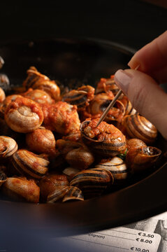 Hand serving escargot with sauce using toothpick