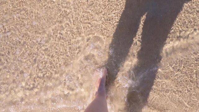 A woman's bare feet on the beach, a woman creating ripples on the surface of the water