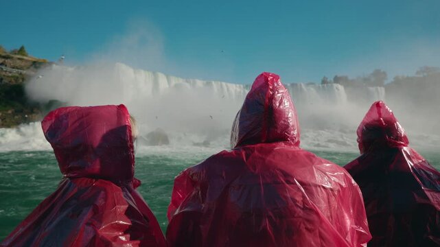 Group of tourists in red rain ponchos observing Niagara Falls waterfall from boat during sightseeing tour