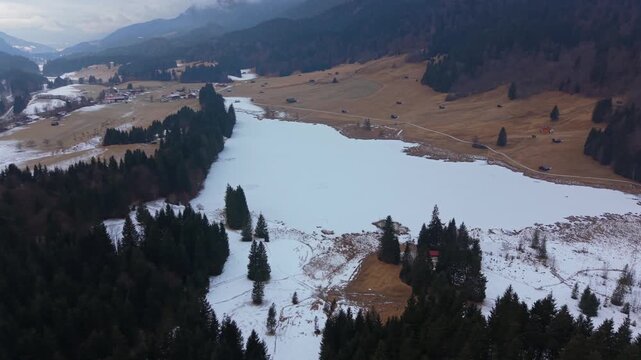 Winter aerial perspective of Geroldsee in Kruen, Upper Bavaria. The Wagenbruchsee is completely covered in snow. A peaceful and popular destination in the Bavarian Alps region.