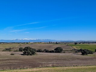 Fototapeta premium Wide view of farmland and snow capped mountains in a clear sky during the day in a rural area