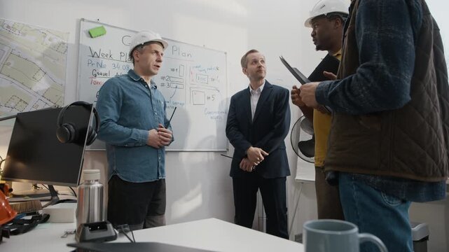 Low angle view of diverse team of construction workers and engineers discussing work by whiteboard in modern office