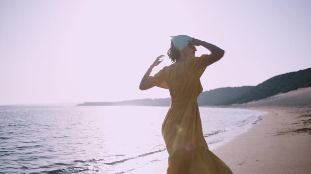 Cheerful Woman in Yellow Dress Enjoying Relaxing Moments by the Ocean at Sunset