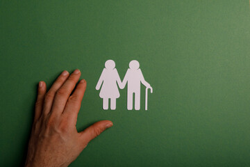 An image of an elderly couple cutout on a green background with a hand reaching towards them,...