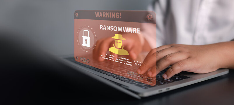Businessman using laptop with ransomware warning alert and hacker icon. Concept of cyber attack, malware infection, data encryption threat, network security breach, and digital protection.