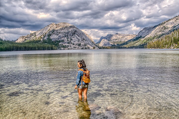 A woman stands in a lake wearing a blue jacket and shorts