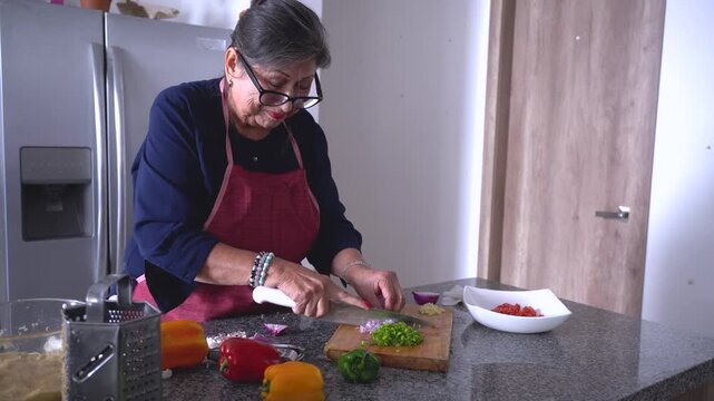 Elderly hispanic woman chopping vegetables in kitchen