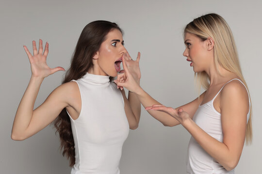 Studio shot of two young women friends having an argument and trying to calm down on gray background