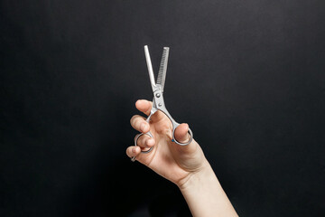 Fototapeta premium Hand Holding Thinning Hair Scissors Against Dark Background