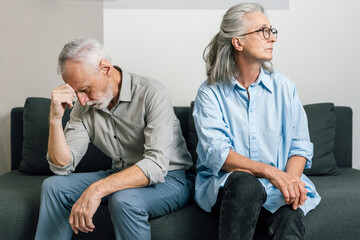 Elderly man and woman upset sitting separately on sofa