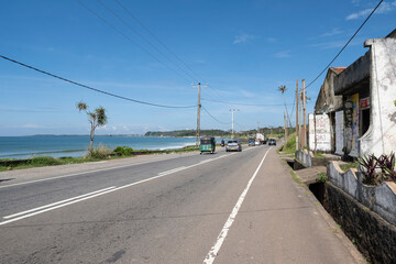 12.06.2025 Matara, Sri Lanka. Traditional colorful tuk-tuk taxi driving on the scenic coastal road between Matara and Dondra, Sri Lanka. Tropical palm trees and Indian Ocean in the background.