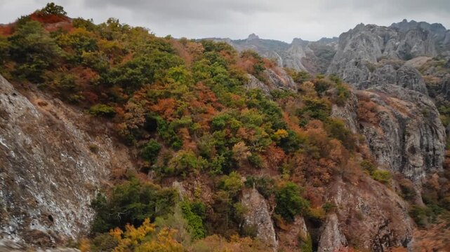 Man stands among rocks and holds control panel of drone, which flies off into distance and shows mastabas of mountains and nature of Georgia, dynamic shot that conveys mastery of hiking and trekking
