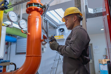 Asian engineer wearing glasses working in the boiler room,maintenance checking technical data of...