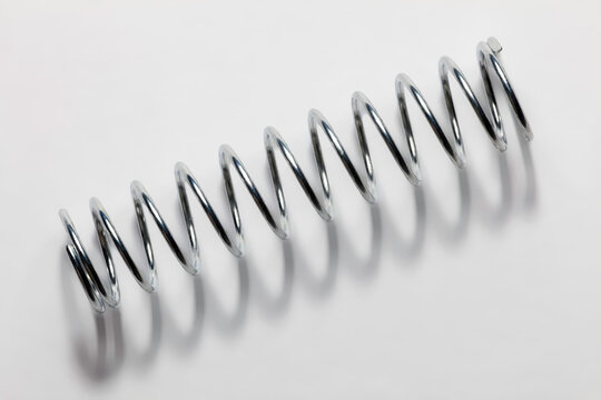 Close-up of a metallic compression spring on a light surface, emphasizing coil geometry, elasticity, and mechanical engineering concepts.