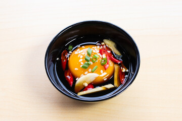 Pickled egg yolk in soy sauce topped with sesame seeds, chili, and garlic in a black bowl, a...