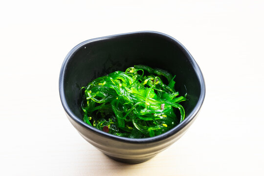 Traditional Japanese Chuka Wakame seaweed salad with sesame seeds in a black bowl, served on a light wooden background, a healthy appetizer.