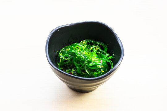 Traditional Japanese Chuka Wakame seaweed salad with sesame seeds in a black bowl, served on a light wooden background, a healthy appetizer.