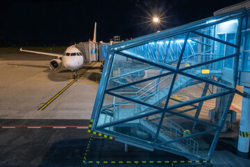Naklejka premium Illuminated boarding bridge with stairs at airport terminal at night