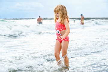 Happy Child, Little Preschool Girl in Swimmsuit Running And Jumping In The Waves During Summer Vacation On Exotic Tropical Beach. Family Journey On Ocean Coast.