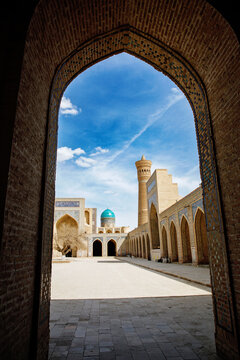 Courtyard view of the Mir-i Arab Madrasa framed by the grand iwan of the Kalyan Mosque in Bukhara, Uzbekistan, showcasing iconic Islamic architecture and blue-tiled domes.