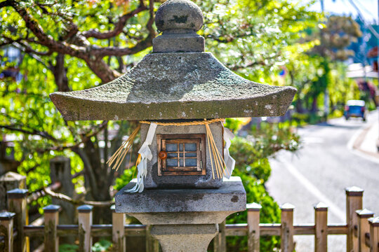 Traditional Japanese stone lantern with shimenawa rope and paper shide on sunny street near shrine in historic town, Japan