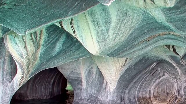 Waves gently lap against the mesmerizing Marble Caves as sunlight dances on the colorful stone. Discover nature's artistry carved over centuries in the breathtaking depths of Patagonia.