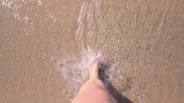 Bare feet of an overweight woman on the beach, woman walking along the shore, creating splashes