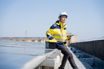 Engineer inspecting solar panels on rooftop with handheld device under clear blue sky © zhu difeng